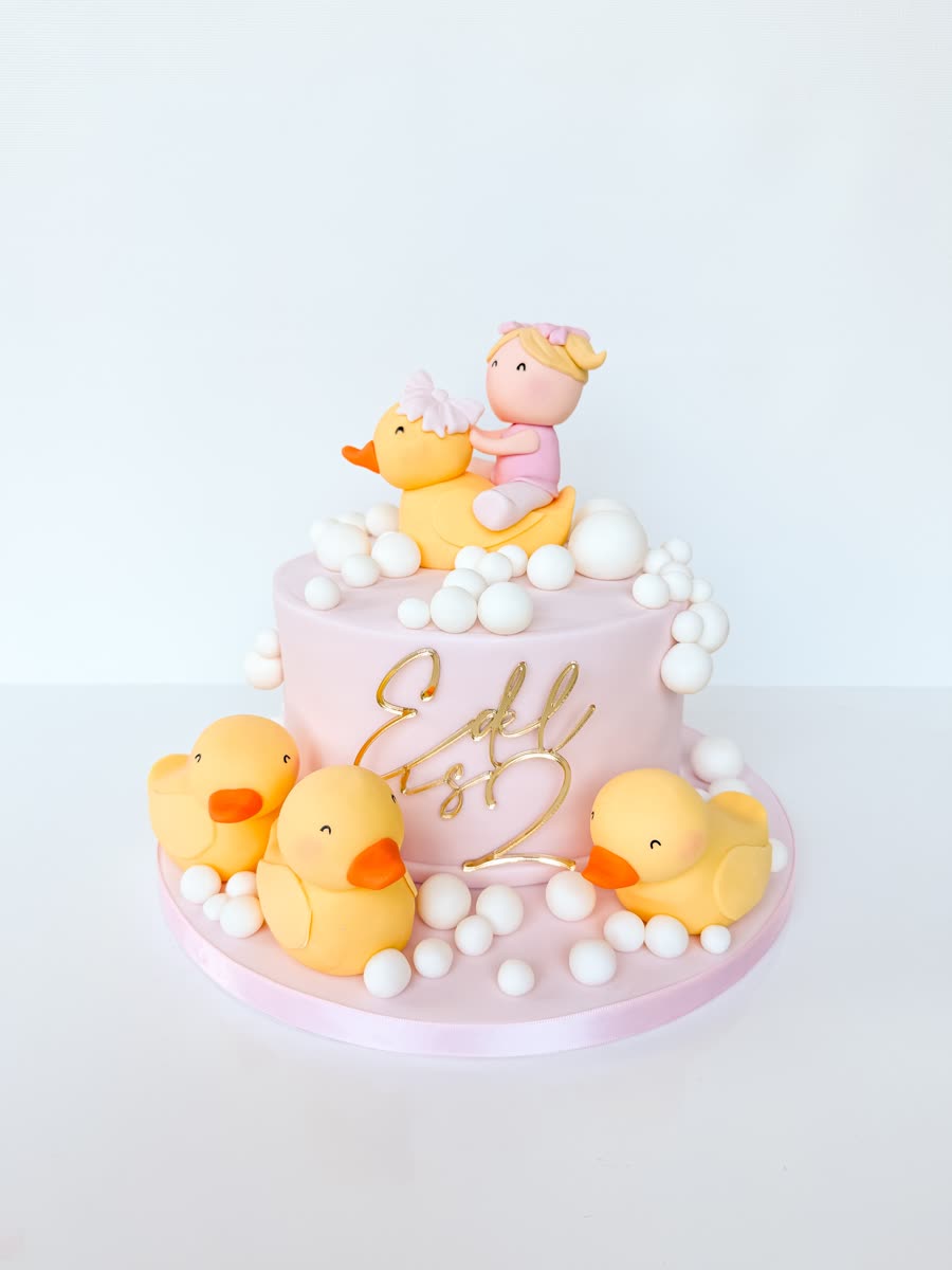 Pink celebration cake topped with fondant rubber ducks, bubbles and a baby figure