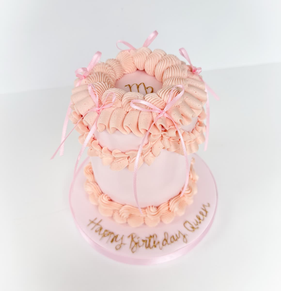 Pink two-tier buttercream birthday cake decorated with ribbon bows
