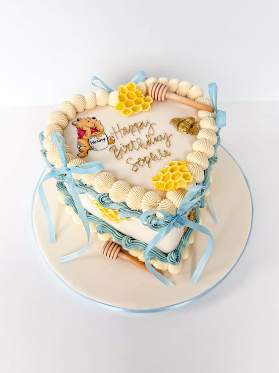 Heart-shaped Winnie the Pooh birthday cake with honeycomb details and blue buttercream bows